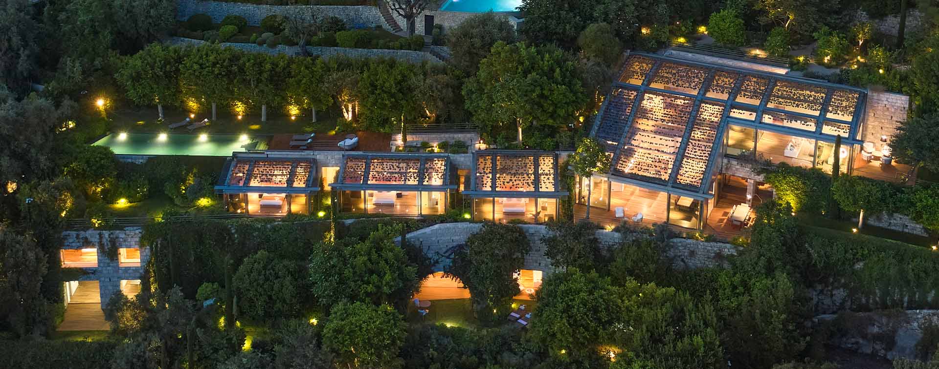 Aerial view of a lit-up modern villa surrounded by trees at nighttime