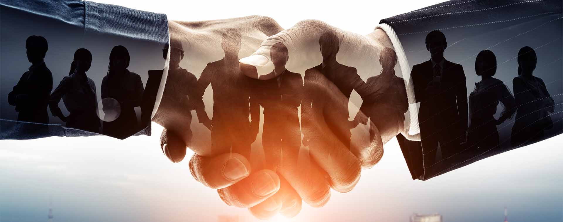 Digital composite image of two hands shaking, containing the shadow of businesspeople above a city skyline.