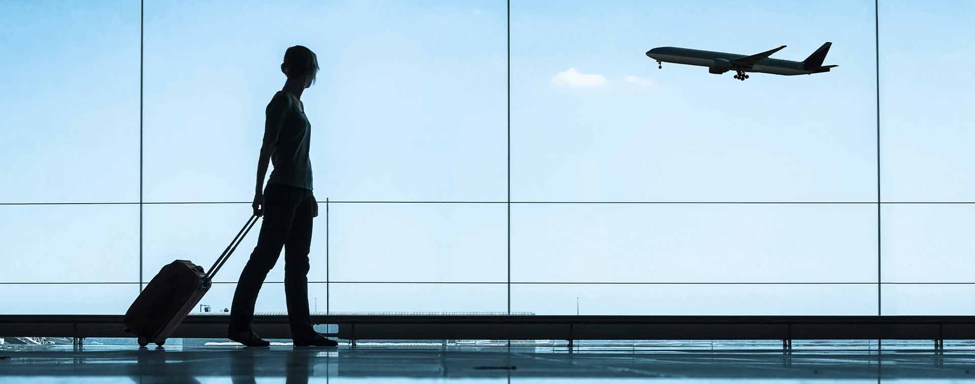 Woman dragging a suitcase looking out of a window at a plane taking off