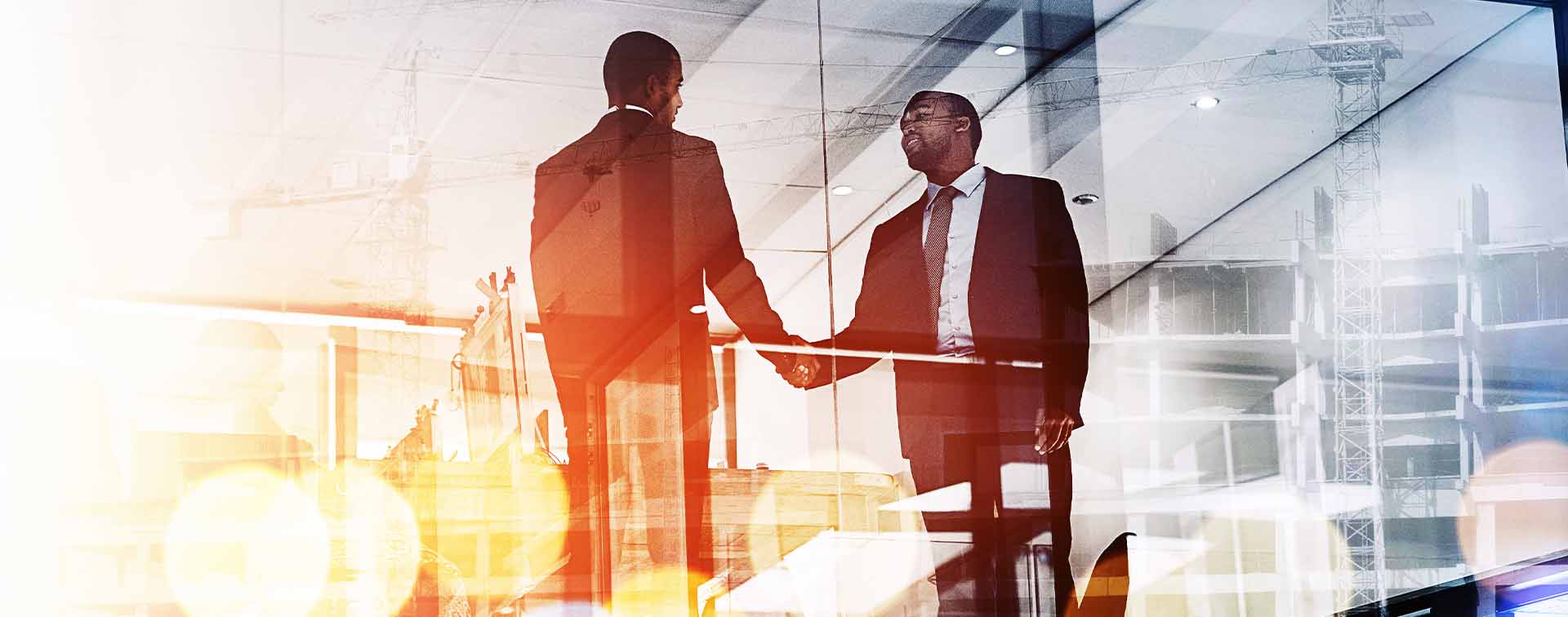 Glass building shot of wwo men shaking hands at sunset.