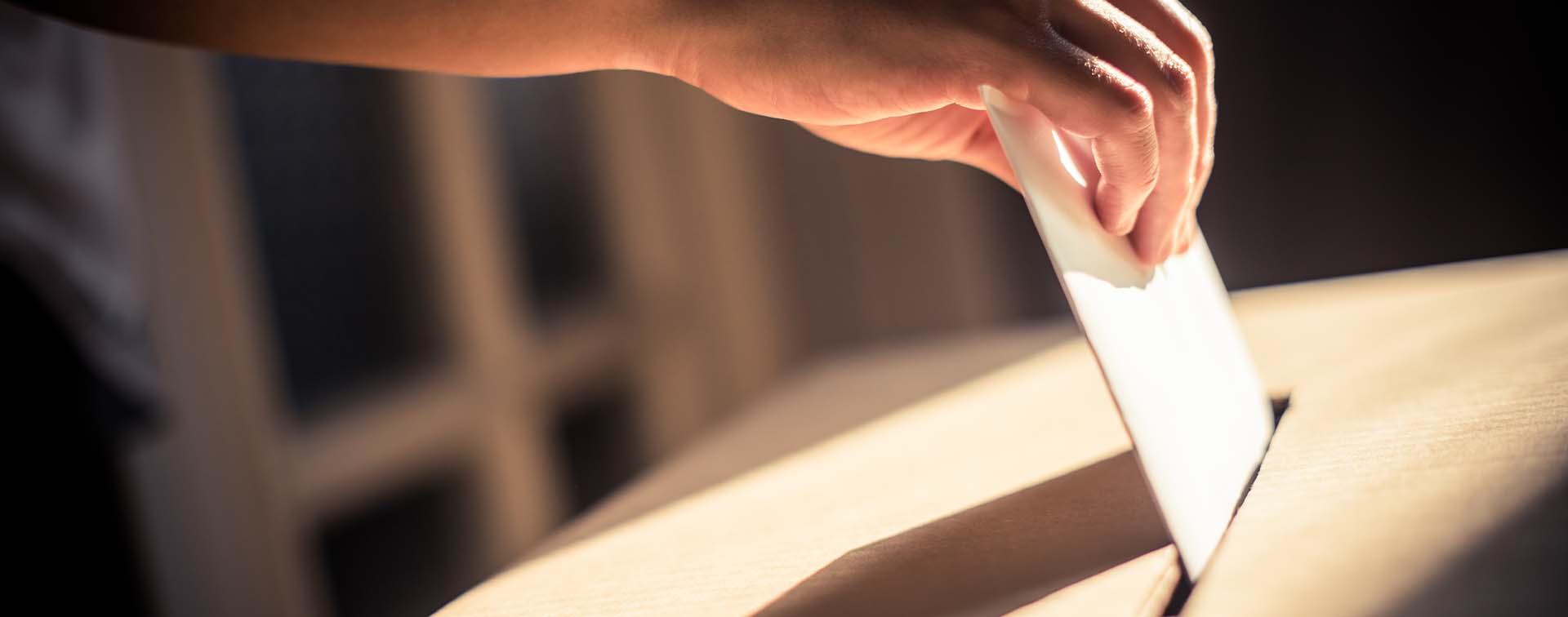 Hand posting a ballot into a ballot box