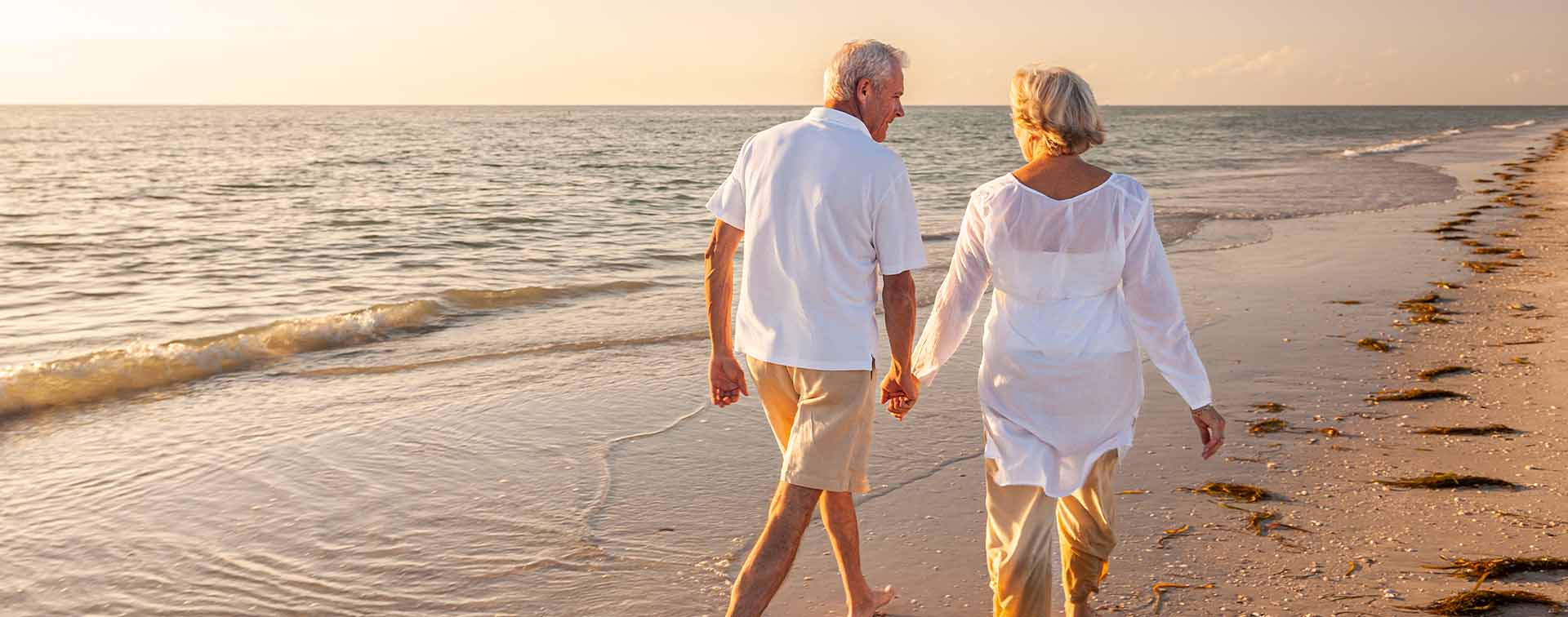 Happy Senior Old Retired Couple Walking Holding Hands on Beach at Sunset