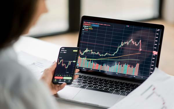 Successful Smart female crypto investor analyzing charts on laptop and phone for trading