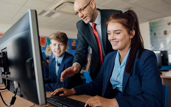 A teacher explains something on a computer to two high school students