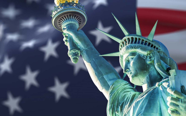 The statue of liberty with blurry American flag waving in the background