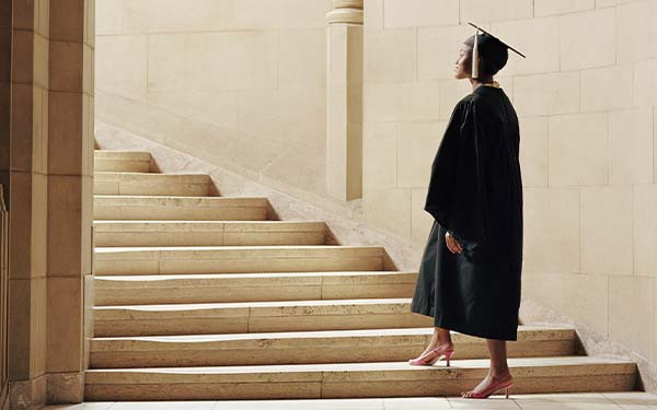 Women wearing graduation cap and gown, ascending staircase, rear view